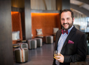 Man smiling holding a cocktail wearing a bowtie and pocket square