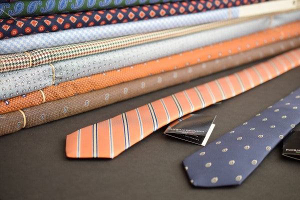 Two neckties on a table with bolts of fabric in the background