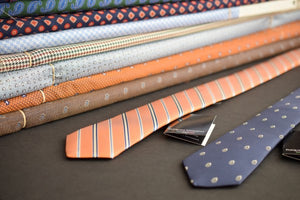 Two neckties on a table with bolts of fabric in the background